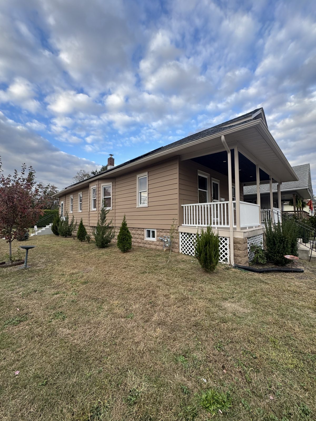 Freshly painted tan vinyl siding ranch home with white covered porch railings and stone-look skirting