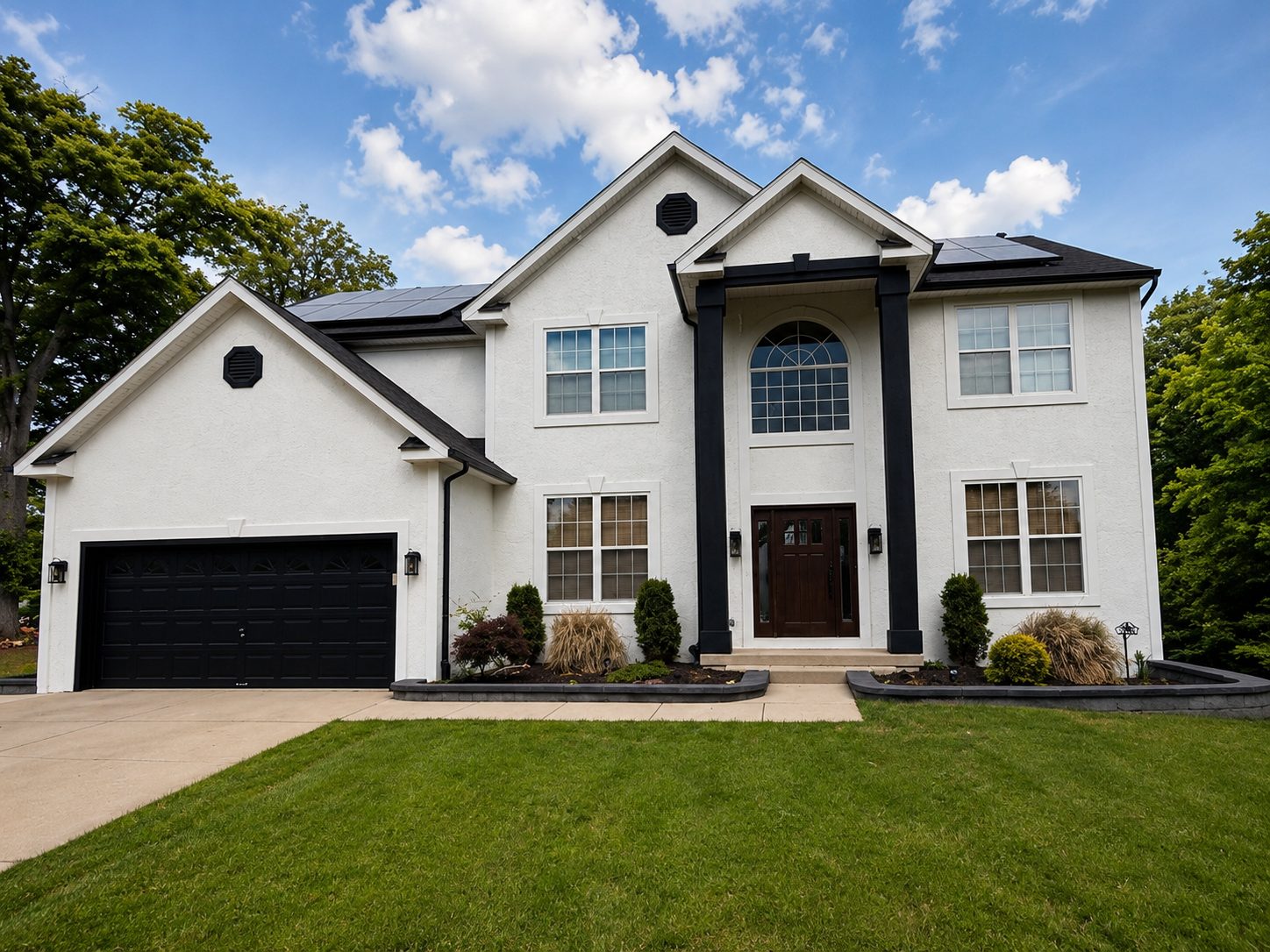 Freshly painted white stucco two-story home with black trim, columns, and garage door
