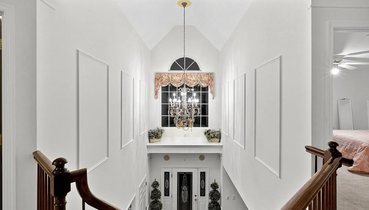 Freshly painted elegant white staircase landing with wainscoting panels and chandelier